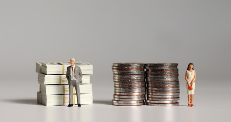 A pile of hundred dollar bills and coins with miniature people. The concept of gender pay gap.