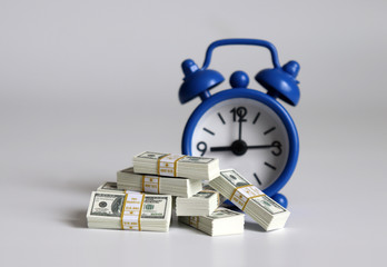 Money bundles of hundred dollars in front of a blue alarm clock.