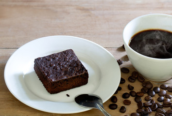 Fototapeta na wymiar Brownie cake in white dish and black coffee in cup on wooden table