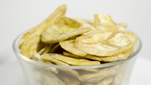 Detail of banana chips in a glass jar rotating on a white background. Flat plane. High angle shot