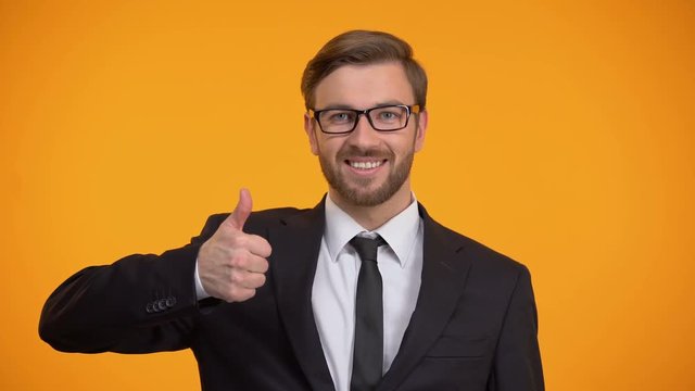 Happy man in suit showing thumbs up and winking at camera, good proposition