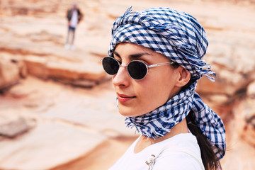 The face of recency. Young cute girl with a smooth perfect skin under the bright lights of the sun in the kerchief of black, white and blue colors and black oval sunglasses framed with silver.