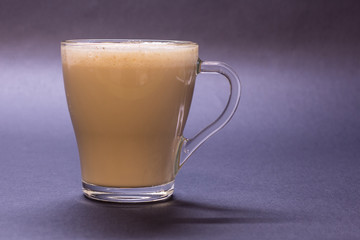 Transparent glass cup with coffee on violet background. Bright tone, soft focus