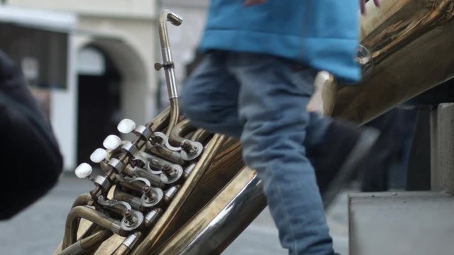 A giant brass instrument lies against stair on the street as a child steps past in Melnik, Czech Republic.