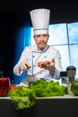 Cook in white uniform holds in his hands a piece of chicken in the spices