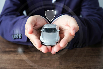 Business man hands holding car and shield icon , car insurance concept.