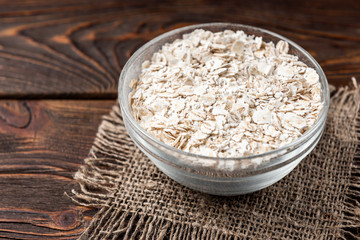 Pearl barley flakes on dark wooden background.
