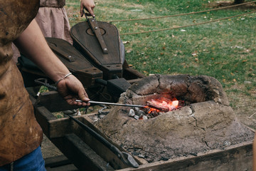 Blacksmiths in ancient clothes poking burning coals in medieval furnace and squeezing bellows to...