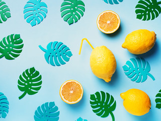 Lemon fruit with straw on blue background pattern, lemonade theme with monstera leaves