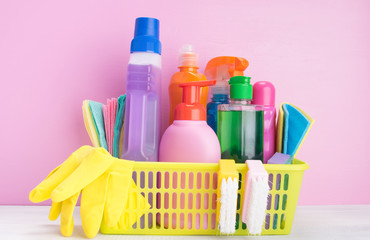 on the table, on a pink background, there is a yellow basket with a set of items for cleaning with rubber gloves and liquids, for disinfection
