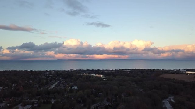 Rising drone footage before a landscape with a view of the water at sunset with huge puffy pink clouds.
