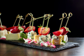 Cheese plates served with strawberry and grapes on black slate.