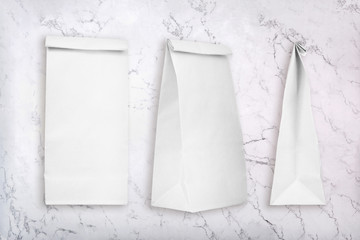 Blank white paper bags on white marble texture. White paper bags fit for lunch, party or wedding favors