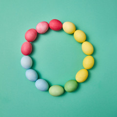 Round frame of multicolored, painted Easter eggs on a green background with copy space for text. Flat lay