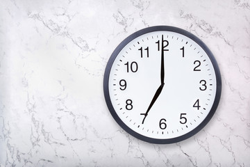 Wall clock show seven o'clock on white marble texture. Office clock show 7pm or 7am on marble background