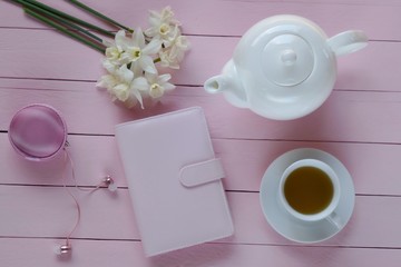 Spring tea.Flat lay.pink notebook, cup of tea and white daffodils flowers ,headphones on a  pink...