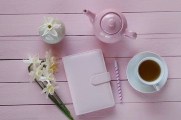 Spring tea.Flat lay.Spring to-do list.pink notebook, cup of tea and white daffodils flowers ,headphones on a  pink wooden  background.top view, copy space.Spring mood