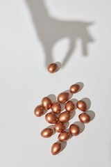 The shadow of the hand takes a golden painted egg on a gray background with copy space for text. Profit concept. Flat lay