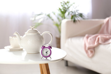 Alarm clock, teapot and cup on table in light room