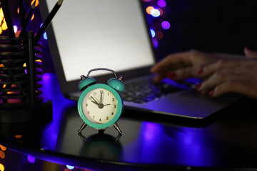 Alarm clock on table of woman working with laptop in evening