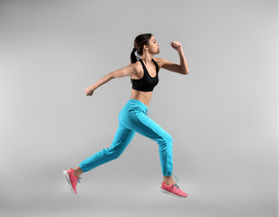 Fototapeta na wymiar Sporty young woman running against light background