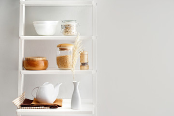 Shelves with kitchenware near white wall