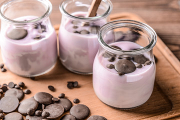 Jars with tasty yogurt and chocolate chips on wooden board, closeup