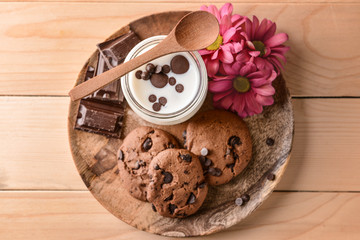 Jar with tasty yogurt and chocolate chip cookies on wooden plate