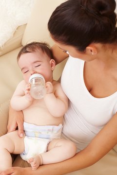 Naked baby with feeding bottle sleeping at mum