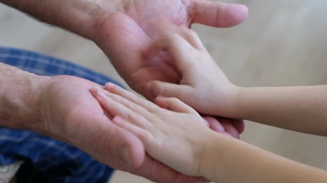 Senior man holding baby's hands, closeup. Two generations