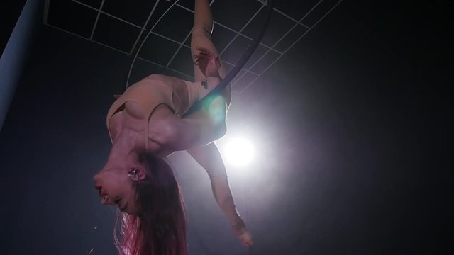 Concept of dance and acrobatics. Young beautiful woman in aerial hoop with color backlight