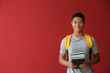 African-American schoolboy with books on color background