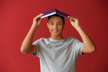 African-American schoolboy with book on color background