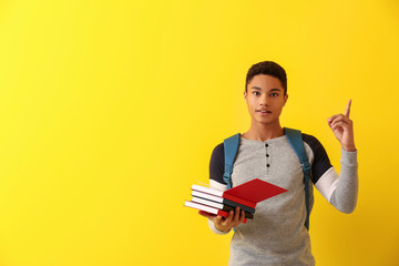 African-American schoolboy with books and raised index finger on color background