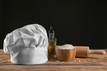 Composition with chef's hat on wooden table against dark background