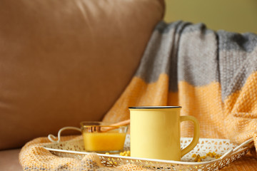 Tray with cup of hot tea and honey on armchair