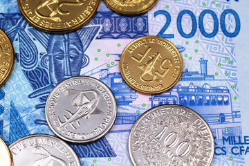 A pile of West African Franc coins, close up on a blue two thousand West African Franc bank note