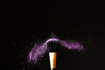 Makeup brush and burst of eyeshadows on dark background