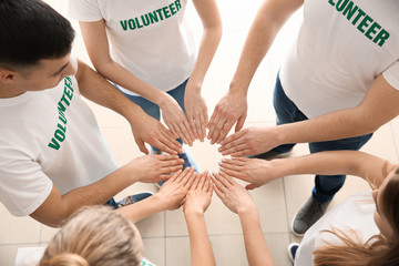 Team of young volunteers holding hands together indoors