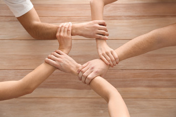 Team of young volunteers holding hands together on wooden background, top view