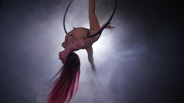 Concept of dance and acrobatics. Young beautiful woman in aerial hoop with color backlight