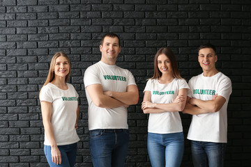 Team of young volunteers against dark brick wall