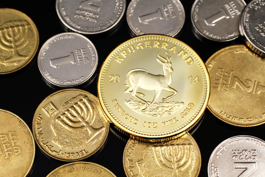 A macro image of miscellaneous coins from Israel with a gold South African Krugerrand on a reflective black background