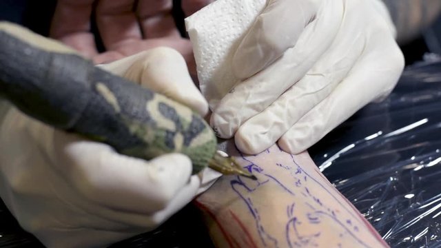 A close up of a tattoo artist makes a tattoo on a man's arm