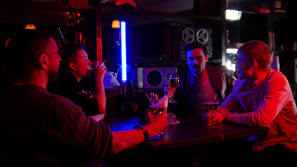 Bar with neon lighting. Group of friends sitting by the table and drinking alcohol