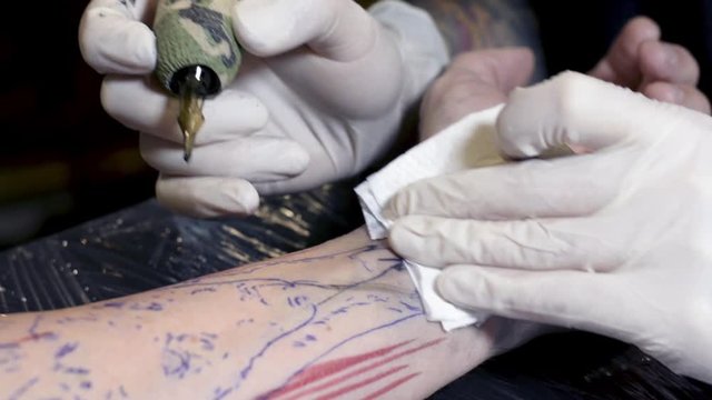 A close up of a tattoo artist makes a tattoo on a man's arm