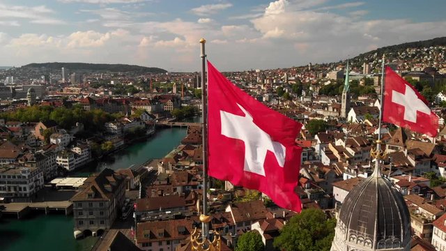 Aerial circling drone shot around Swiss flags on Grossm&uuml;nster church in Z&uuml;rich Switzerland closer