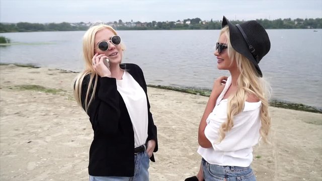 Two pretty girls blondes in glasses walking along the coast, talking and enjoying life