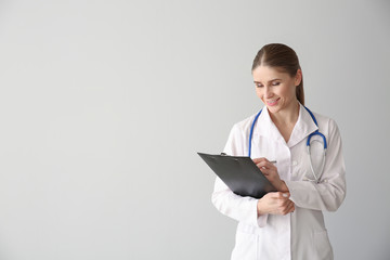 Female doctor with clipboard on light background