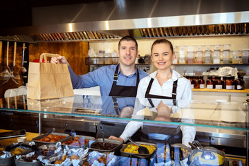 Business restaurant owners smiling behind counter holding paper bag with food order for home...